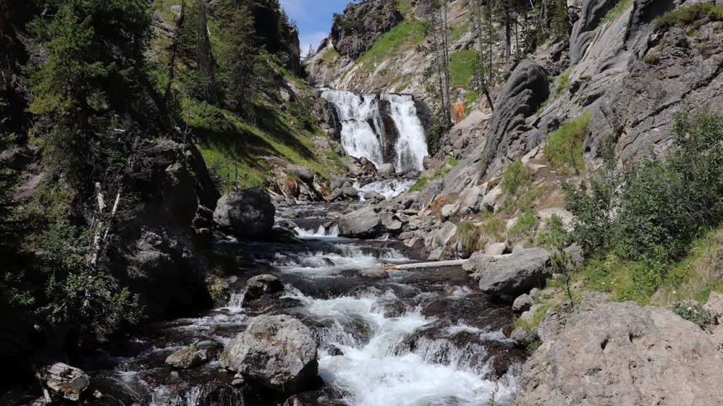 Mystic Falls cascades over a rocky cliff into the Little Firehole River.