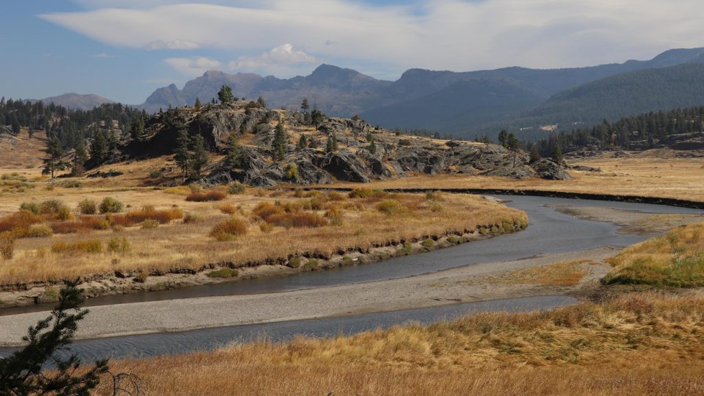 Slough Creek curves through golden meadow grass below rocky hills and distant mountains in northeast Yellowstone.